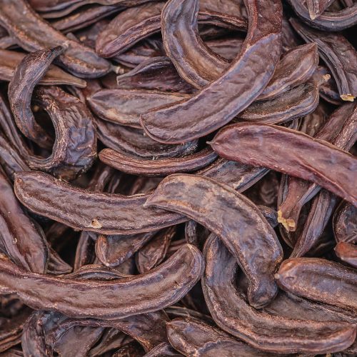 Carob tree pods on a wooden table top view, close-up. Healthy Organic Sweet Carob Pods